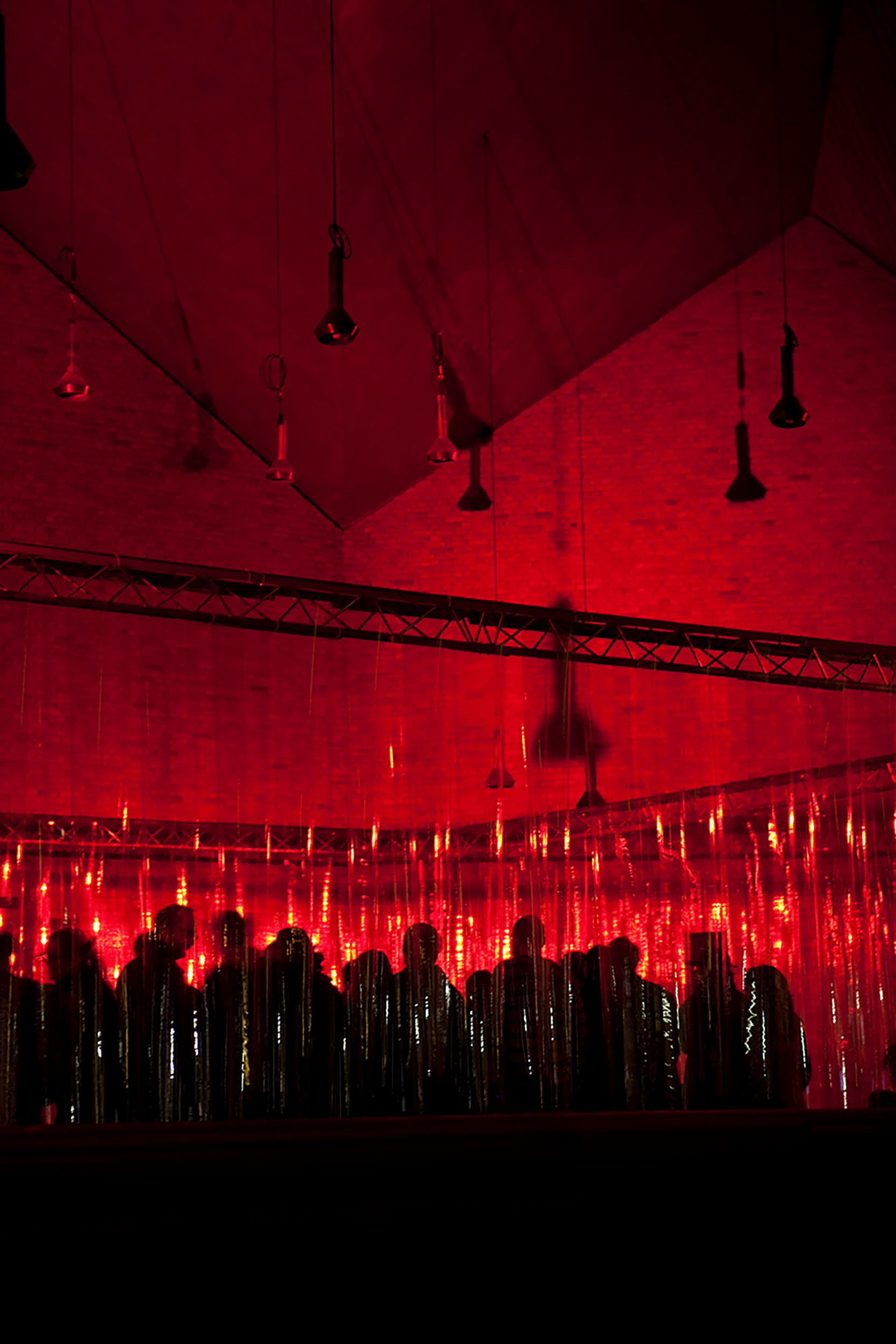 Konzertbesucher hinter PVC Lamellen, eingetaucht in rotes Licht.